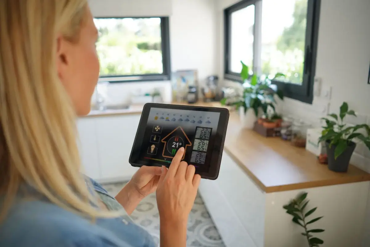 Eine Person nutzt ein Tablet in einer modernen Küche mit Pflanzen im Hintergrund.