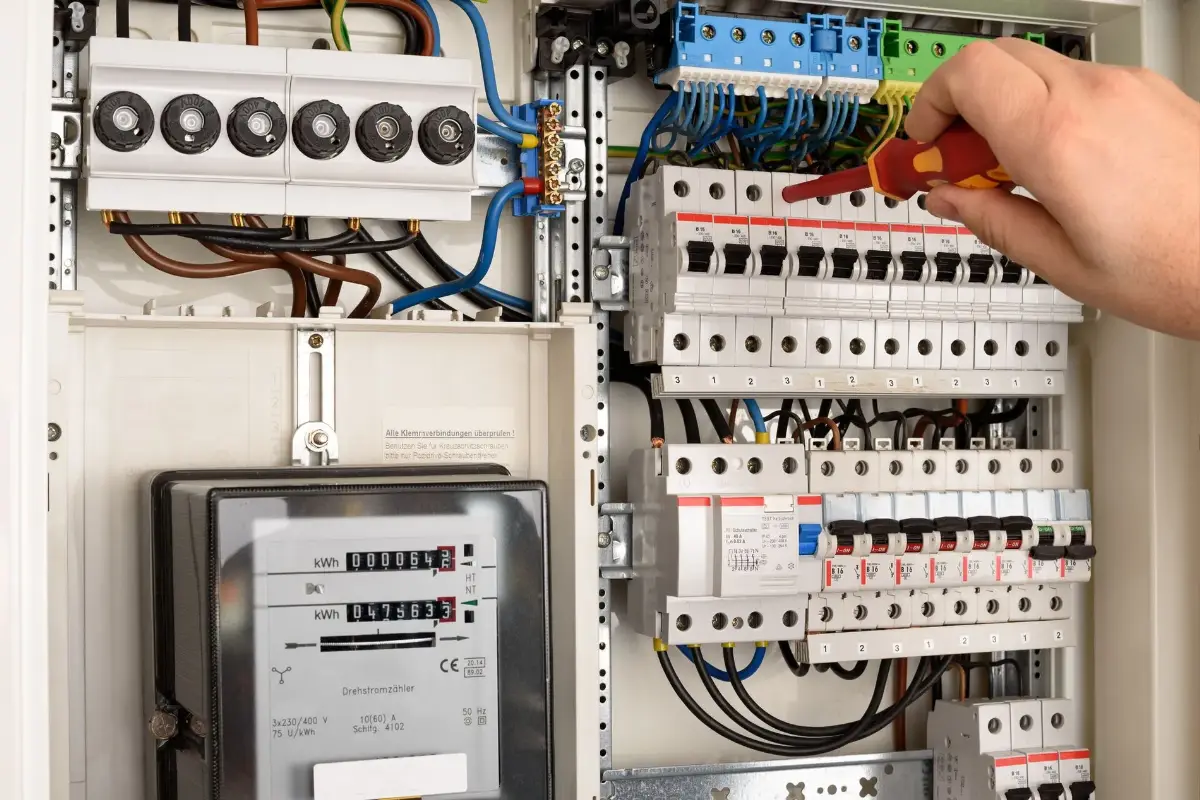 Eine Hand hält einen Schraubendreher in einem Elektroverteilungsschrank.