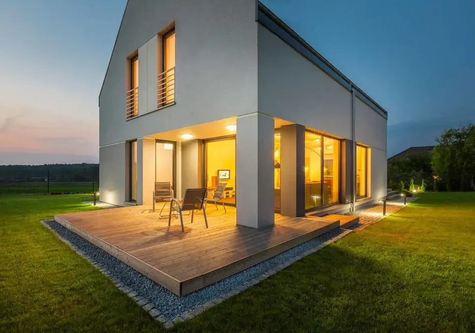 Ein modernes Haus mit großen Fenstern, umgeben von grünem Gras und Abenddämmerung.