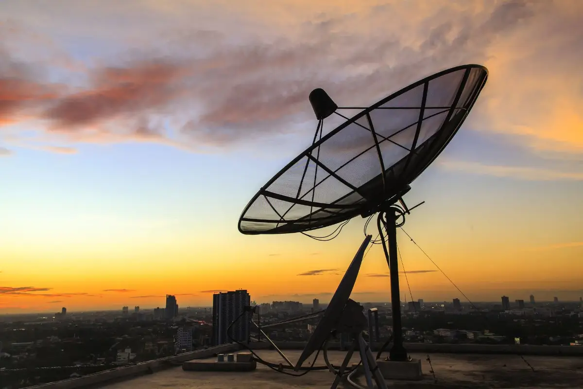 Eine Satellitenschüssel vor einem bunten Sonnenuntergang über einer Stadt.