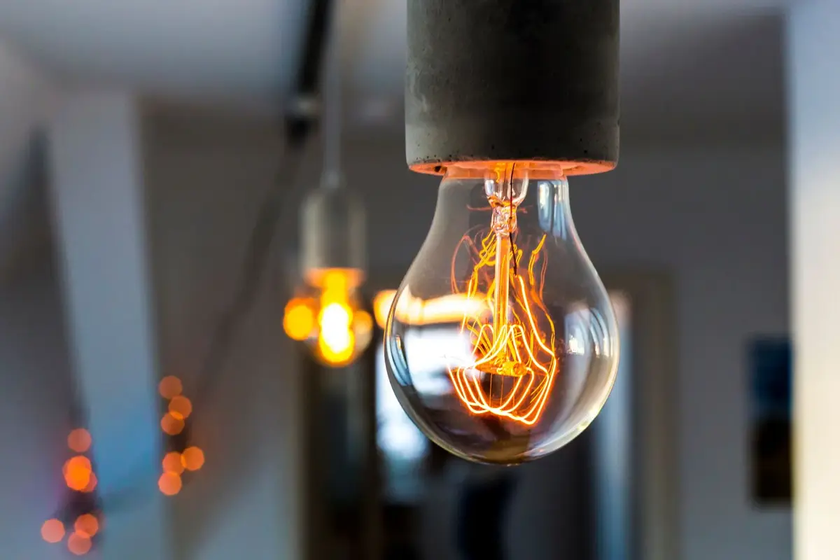Ein leuchtende Glühbirne hängt in einem modernen Raum mit unscharfen Lichtern im Hintergrund.