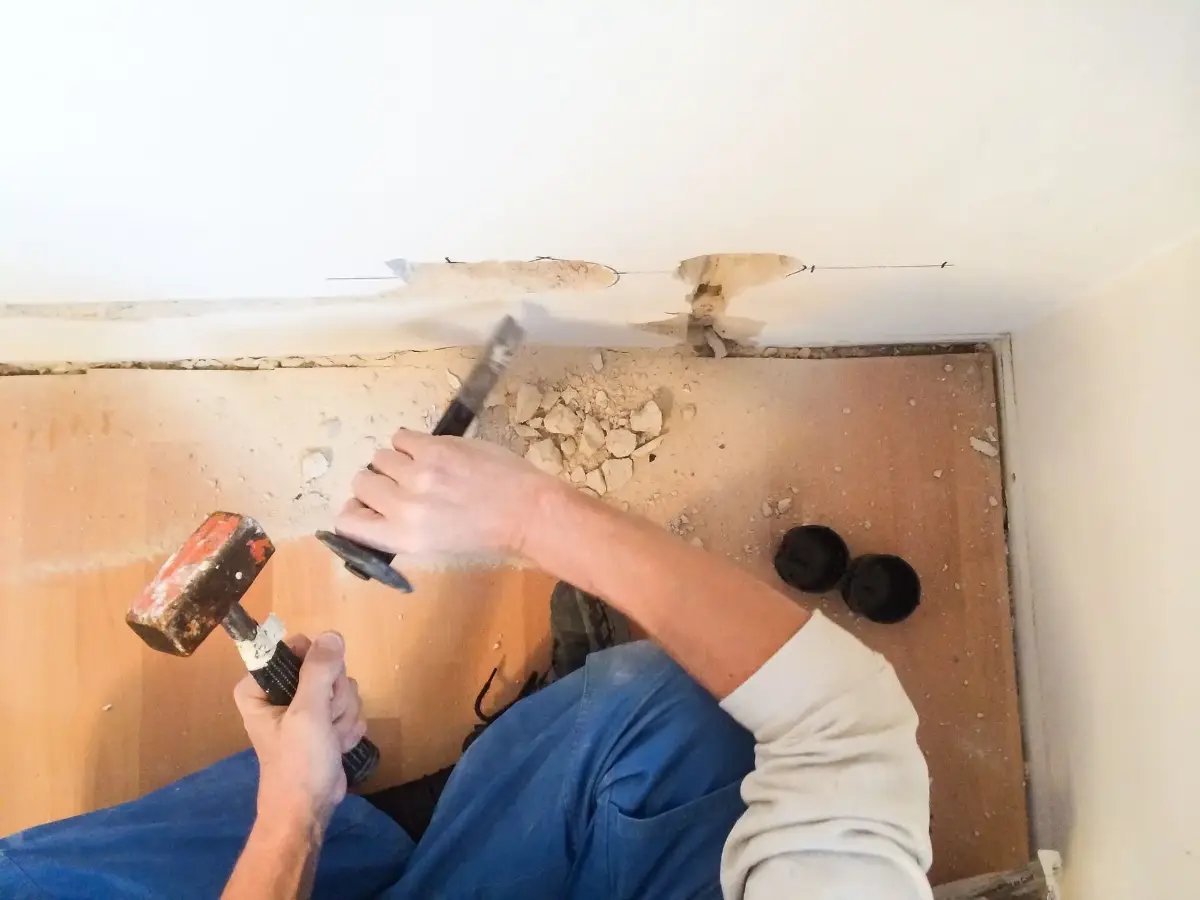 Person bearbeitet eine Wand mit einem Werkzeug, daneben sind Werkzeuge und Sägemehl sichtbar.