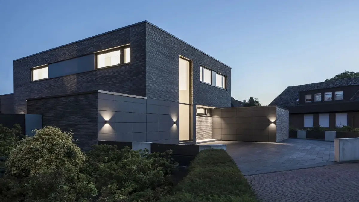 Modernes Haus mit klaren Linien, großen Fenstern und sanfter Außenbeleuchtung bei Dämmerung.