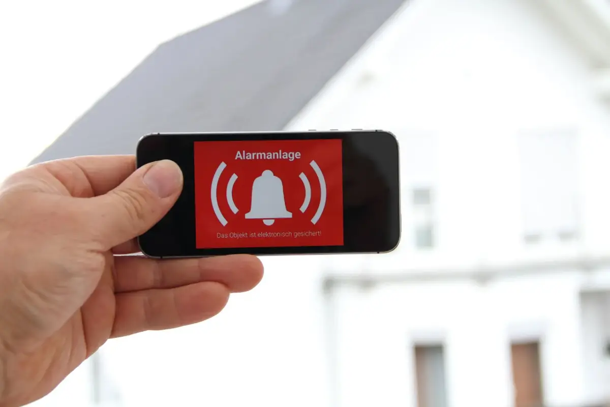 Ein Smartphone zeigt eine Alarmgrafik mit einem Glockensymbol vor einem Haus.