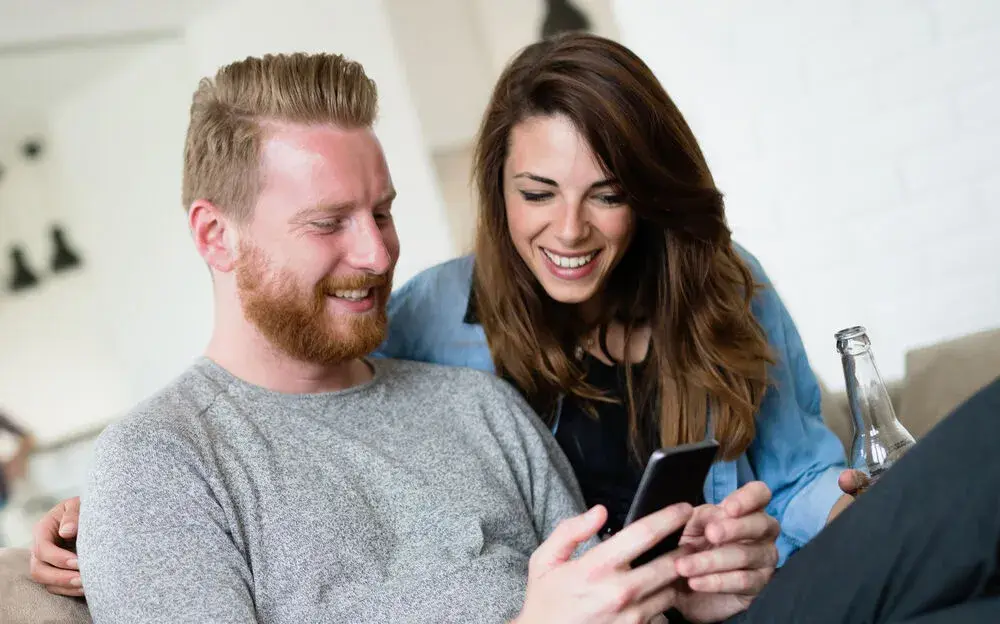 Lachendes Paar betrachtet gemeinsam ein Handy.